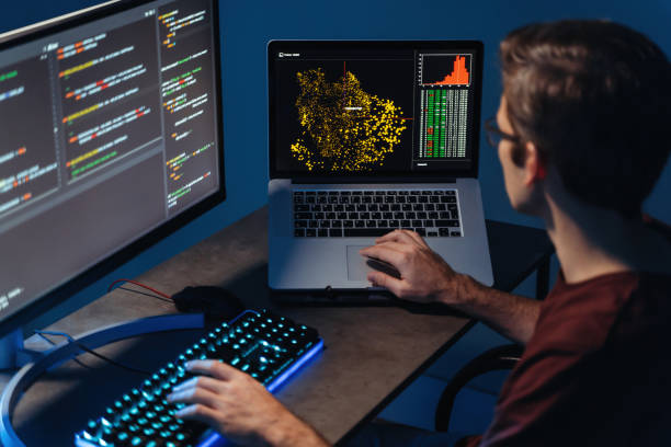 Back view of busy male data scientist typing on keyboard on pc and laptop with programming code on screen, using php language for coding app, sitting at home office